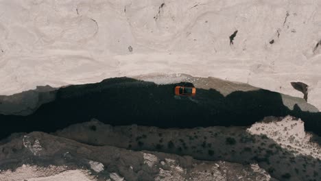 Orange-4x4-offroad-SUV-driving-in-canyon-river,-aerial-top-down-view