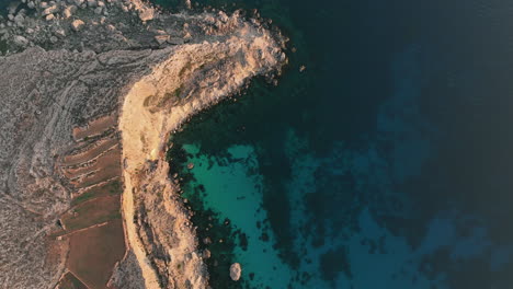 Sunset-drone-footage-capturing-the-seaside-cliffs-and-crystal-clear-water-on-the-coastline-of-Malta