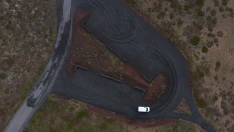 Car-turning-on-dark-gravel-surface-parking-lot-in-Iceland,-top-down