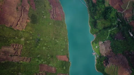 An-ascending-drone-shot-of-a-calm-turquoise-river-reveals-a-reservoir