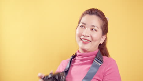 Fröhliche-Begeisterte-Asiatische-Frau-Mit-Einer-Digitalkamera-Für-Reisen-Vor-Gelbem-Hintergrund