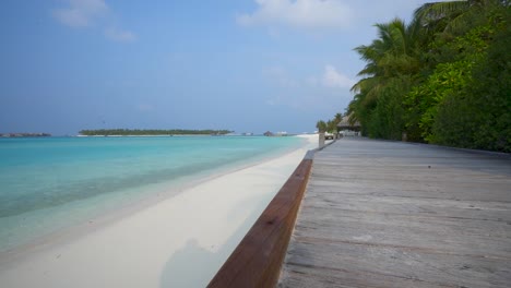Tropical-beach-with-raised-wooden-walkway-next-to-green-trees-along-ocean