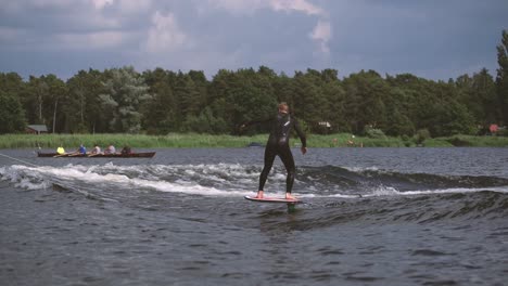 Man-on-foil-surfing-in-wave-with-rower-in-background