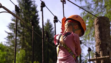 6-year-old-european-girl-passing-wooden-treetop-bridge-inside-Voss-climbing-park---Summer-vacation-activity-with-safety-equipment-and-beautiful-sunlight-coming-from-behind---Norway-slow-motion
