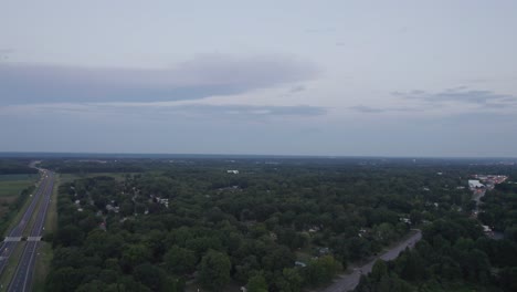 Aerial-drone-forward-moving-shot-over-town-houses-surrounded-by-green-trees-beside-the-roadside-after-sunset