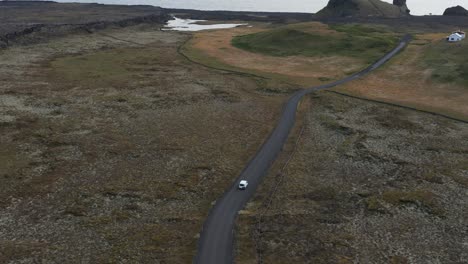 Car-drives-on-remote-road-in-volcanic-landscape-towards-edge-of-Reykjanes-peninsula