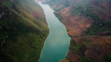 An-aerial-shot-looking-down-at-a-turquoise-reflective-river-reveals-a-dam-in-the-distance