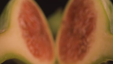 Halbierte-Frische-Reife-Feigenfrucht,-Dolly-Makro-Nahaufnahme-Sondenlinse-Defokussiert-Studioaufnahme-Von-Scheiben-Süßen-Weichen-Rötlichen-Fleisches-Mit-Knusprigen-Samen-Im-Inneren-Und-Grüner-Haut