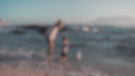 Blurred-shot-of-a-caucasian-mother-with-her-toddler-in-the-beach-playing-with-the-sea-waves-and-looking-into-the-ocean