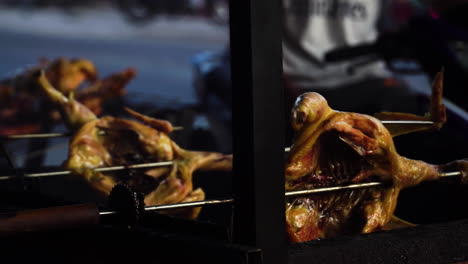 Grilling-whole-duck-on-spit-spinning-above-bbq-grill-next-to-street