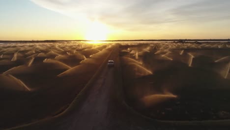 Pickup-car-cross-agricultural-farmland-irrigated-by-sprinklers-at-sunrise