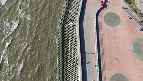 Aerial-drone-flight-along-the-coastline-of-Blackpool-looking-down-from-above-and-slowly-panning-upwards-to-reveal-the-long-coast-and-its-piers-with-the-tower-in-the-distance