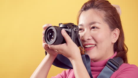 Junge-Asiatische-Frau,-Die-In-Rosa-Kleidung-Mit-Einer-Digitalkamera-Vor-Einem-Isolierten-Gelben-Hintergrund-Mit-Kopierraum-Für-Werbung-Spielt-1