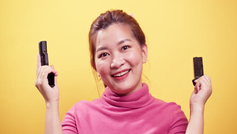 Close-up-Smiling-Asian-woman-checking-handgun-to-safety-for-ammo-on-bright-yellow-background-1