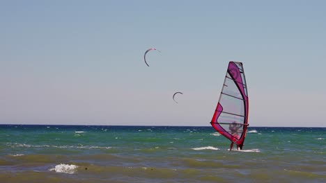 Windsurfista-En-El-Mar-Mediterráneo-En-Cámara-Lenta,-Con-Kitesurfistas-En-El-Fondo