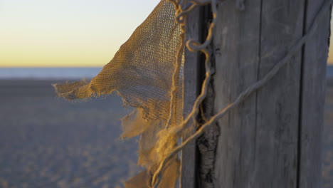 Beautiful-Shot-Of-An-Old-Fishing-Net-Stranded-At-A-Beach-Near-Water-Sunset-Slow-Motion