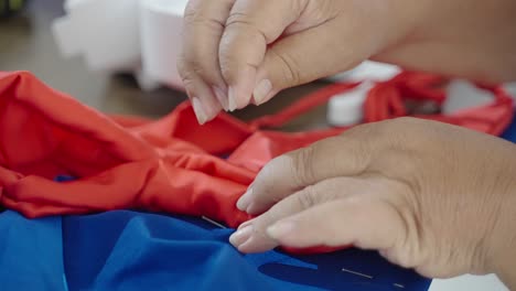 Sastre-Cose-Textiles-Rojos-Y-Azules-Juntos,-Primer-Plano-En-Las-Manos-De-La-Mujer