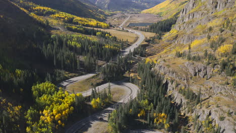 Aerial-shot-panning-up-of-beautiful-winding-Colorado-mountain-roads-and-bright-yellow-and-orange-aspen-trees-during-autumn-in-the-San-Juan-Mountains-along-the-Million-Dollar-Highway-road-trip