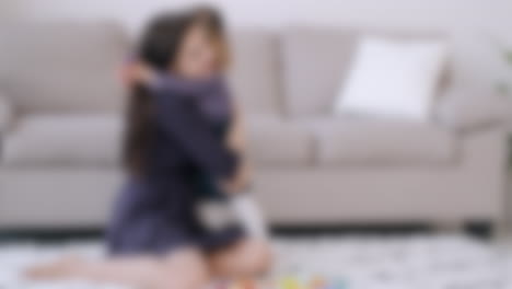 Blurred-shot-of-a-mother-and-her-little-daughter-hugging-and-playing-in-the-living-room,-motherhood-concept-background