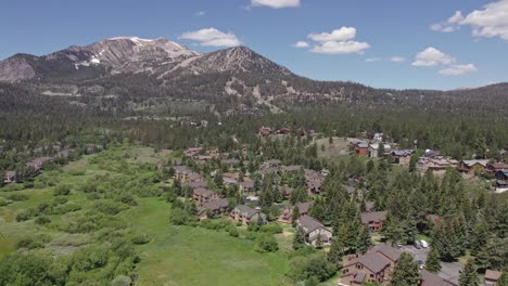 4k-drone-footage-slow-camera-rotation-of-beautiful-Mammoth-Mountain-in-the-summertime-with-a-view-of-a-lush-green-meadow-and-cabins