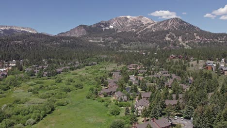 4k-drone-footage-pan-to-the-left-of-beautiful-Mammoth-Mountain-in-the-summertime-with-a-view-of-a-lush-green-meadow-and-cabins