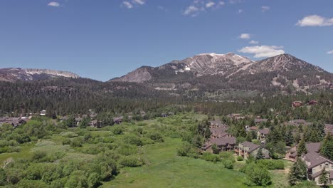 4k-drone-footage-camera-tilt-up-of-beautiful-Mammoth-Mountain-in-the-summertime-with-a-view-of-a-lush-green-meadow-and-cabins