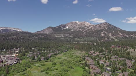 4k-drone-footage-slow-pan-right-of-beautiful-Mammoth-Mountain-in-the-summertime-with-a-view-of-a-lush-green-meadow-and-cabins