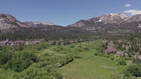 4k-drone-footage-slow-zoom-out-rotation-of-beautiful-Mammoth-Mountain-in-the-summertime-with-a-view-of-a-lush-green-meadow-and-cabins