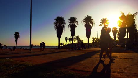 Silhouette-Von-Menschen,-Die-Während-Des-Sonnenuntergangs-In-Brasilia,-Brasilien,-Auf-Dem-Bürgersteig-Am-Meer-Spazieren-Gehen