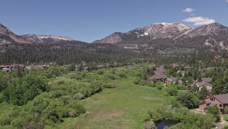 4k-drone-footage-camera-tilt-down-of-beautiful-Mammoth-Mountain-in-the-summertime-with-a-view-of-a-lush-green-meadow-and-cabins-1