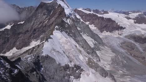 Aerial-view-from-drone-over-snow-in-valley-tilt-up-to-reveal-steep-slopes-and-peaks-of-mountains-in-the-Alps