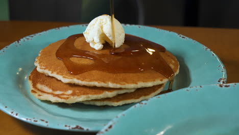 Drizzling-warm-maple-syrup-over-buttered-stack-of-fluffy-buttermilk-pancakes,-slow-motion-slider-4K