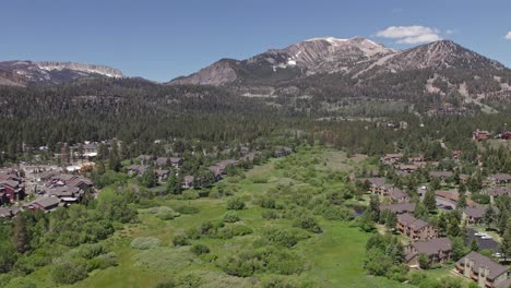 4k-drone-footage-slow-pan-right-and-zoom-out-of-beautiful-Mammoth-Mountain-in-the-summertime-with-a-view-of-a-lush-green-meadow-and-cabins
