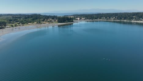 Aerial-view-of-Freeland,-Washington's-bay-of-calm-water-with-three-kayakers-playing-in-the-water-below