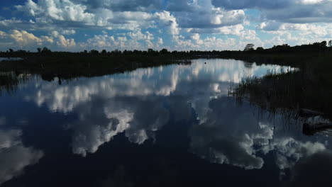 Wide-shot-with-a-slow-jib-down-revealing-a-pond-surface-with-majestic-clouds-reflecting-in-the-water
