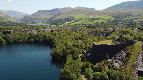 Aerial-view-Welsh-woodland-slate-mining-shaft-and-quarry-lake-orbiting-Snowdonia-mountain-valley