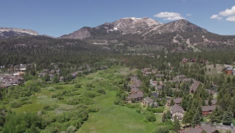4k-drone-footage-camera-pan-right-of-beautiful-Mammoth-Mountain-in-the-summertime-with-a-view-of-a-lush-green-meadow-and-cabins