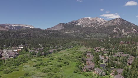 4k-drone-footage-camera-tilt-down-of-beautiful-Mammoth-Mountain-in-the-summertime-with-a-view-of-a-lush-green-meadow-and-cabins
