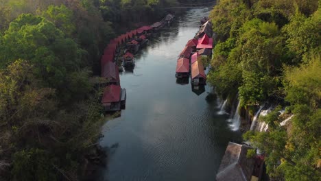 Drone-shot,-flying-over-a-river-in-Thailand-in-the-middle-of-the-jungle,-with-waterfalls-and-a-charming-floating-village-on-the-side-of-the-river---Sai-Yok-National-Park---the-province-of-Kanchanaburi