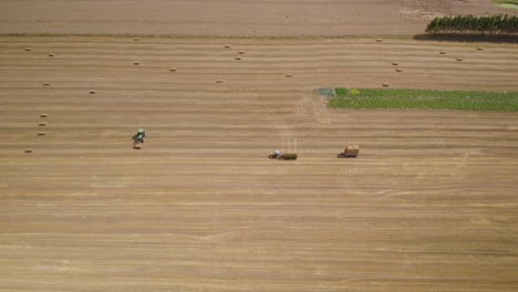 Farmers-working-on-a-hay-field,-loading-up-square-bales-in-tractor-trailer