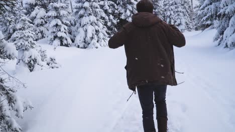 Caucasian-man-in-casual-winter-clothing-walking-in-winter-forest-path-and-putting-on-brown-winter-jacket-to-stay-warm-in-cold-weather