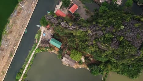 A-descending-aerial-shot-of-property-on-a-canal-in-Tam-Coc,-South-East-Asia,-reveals-a-group-of-small-boats