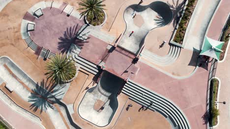 Warm-sunlit-public-skate-park-with-palm-trees-aerial-descending-Birdseye-view