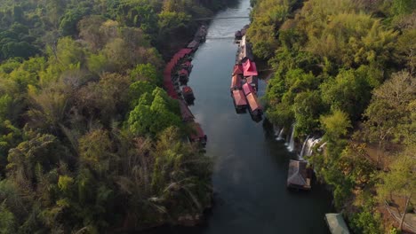 A-rotational-drone-shot-of-a-river-in-the-middle-of-the-jungle,-with-waterfalls-and-a-floating-village-on-the-side-of-the-river