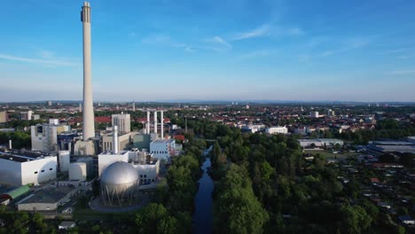 Großer-Runder-Lagertank-Mit-Einem-Hohen-Weißen-Schornstein-Eines-Großen-Kraftwerks-In-Der-Deutschen-Stadt-Braunschweig-An-Der-Oker-Mit-Einem-Klaren-Blauen-Himmel-Im-Hintergrund