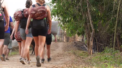 A-group-of-young-and-adventurous-backpackers-is-trekking-and-hiking-toward-a-small-village-with-cows-standing-at-the-end-of-the-road,-in-northern-Thailand-in-the-area-of-Umphang