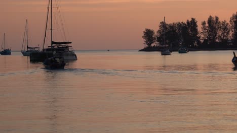 Schöne-Landschaftsaufnahme,-Die-Schimmernde-Sonnenuntergangreflexion-Auf-Ruhiger-Wasseroberfläche-Mit-Fischerboot,-Das-Vorwärts-Kreuzt,-Und-Luxuriöser-Yacht-Einfängt,-Die-In-Der-Bucht,-Langkawi-insel,-Malaysia,-Verankert-Sind