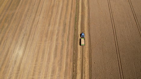Top-View-Of-A-Blue-Farm-Tractor-With-Empty-Trailer-Moving-Across-The-Field