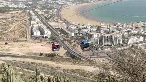 Cable-car-of-the-aerial-tramway-connecting-Oufella-peak-and-Agadir-city-in-Morocco,-overlooking-a-panoramic-view-of-the-beach-1