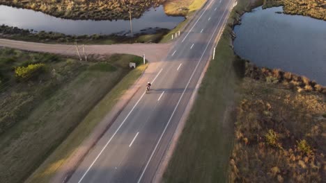 Aerial-view-of-motorcycle-driving-on-coastal-road-near-Atlantic-Ocean-at-sunset-in-Uruguay